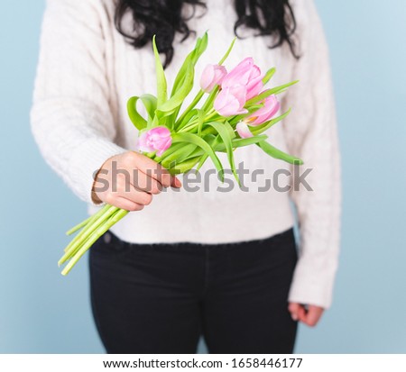 Woman in white sweater and black pants with pink tulip bouquet. Spring concept.