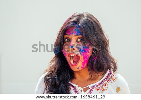 Holi Festival Of Colours. Portrait of happy indian girl in holi color. she dancing and having fun at white wall studio background