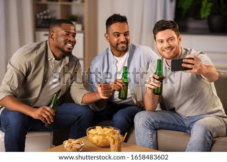 friendship, leisure and people concept - male friends with smartphone taking selfie and drinking beer at home at night