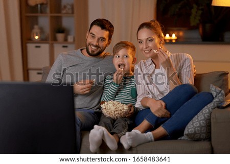 family, leisure and people concept - happy smiling father, mother and little son eating popcorn and watching tv at home in evening Royalty-Free Stock Photo #1658483641