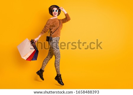 Full size photo of funky lady jump high enjoy season sales shopping carry packs wear fluffy sweater leopard pants boots retro cap clutch bag specs isolated yellow color background