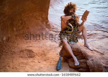 Caveman swiping his primitive touch screen stone tablet outdoors in a weathered rock cave Royalty-Free Stock Photo #1658489662