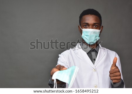young black man in medical field, wearing a white coat and face mask, offering a face mask Royalty-Free Stock Photo #1658495212