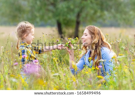 Beautiful hapy baby girl child with young mother wearing casual clothes outdoors having fun and picking flowers in a summer meadow. Concept of a happy family relationship Royalty-Free Stock Photo #1658499496