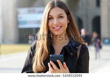 Student girl typing on smart phone out of school looking at camera