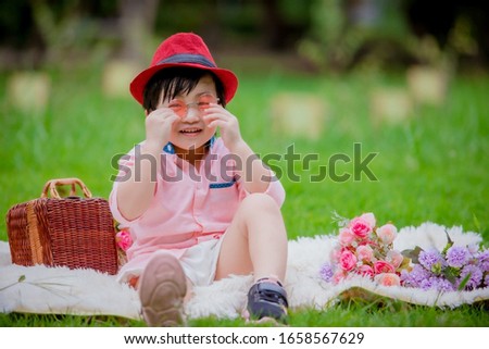 A boy wearing a red hat, wearing sunglasses, smiling on a white hairy crab in a green garden, in front of a green grass, shoes and white fur in a blur.
