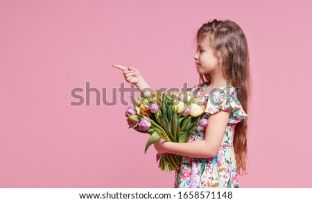 Cute smiling child girl holding bouquet of spring flowers tulips isolated on pink background. Little toddler girl gives a bouquet to mom. Copy space for text. 