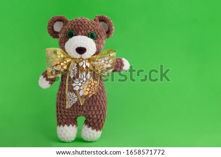 Children's knitted toy bear with bow on a green background