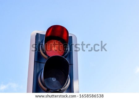 British traffic light/signal illuminated red to indicate to traffic to stop, set against a blue sky on a sunny day.