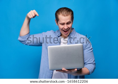A man in casual clothes on a blue background is about to press a button in a laptop with a smile. Close up.