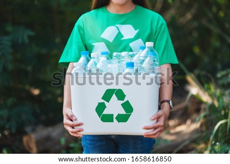 A woman collecting garbage and holding a recycle bin with plastic bottles in the outdoors Royalty-Free Stock Photo #1658616850
