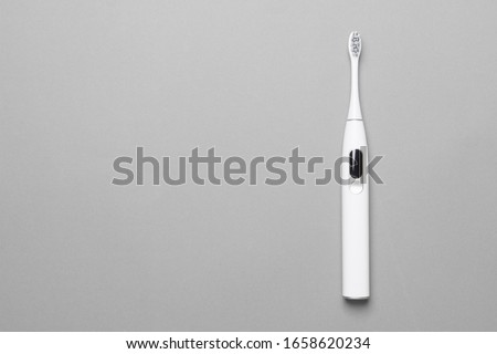 white ultrasonic toethbrush with monitor on grey colored paper background, top view with copy space.