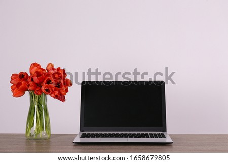Fresh flower composition, bouquet of darwin hybrid tulips with black and white laptop computer, white wall background. Office romance concept. Copy space, close up, top view, flat lay.
