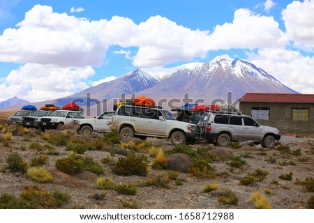 Bolivia, Andes highlands. Off road adventure with 4x4 vehicles the desert.   Arid dry land and in the background mountains and cloudy sky. Vehicles parked for a resting.