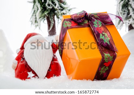 Santa Claus is presenting a big Christmas Gift within a deep covered snow scene.