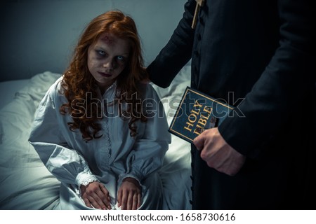 exorcist holding bible and hugging demoniacal girl in bedroom Royalty-Free Stock Photo #1658730616