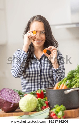 Playful young woman holding slices of carrot in the kitchen - diet vegetable and heath concept.