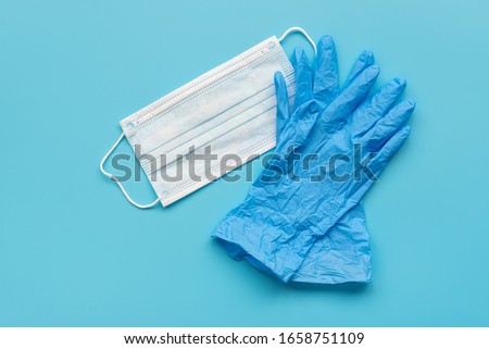 Pair of latex medical gloves and surgical ear-loop mask on blue background. Protection concept Royalty-Free Stock Photo #1658751109
