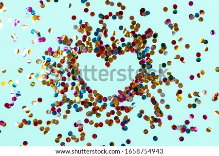Heart shape made of golden colorful confetti splash on blue background. Festive backdrop of sparkles for birthday, valentine's day, carnival