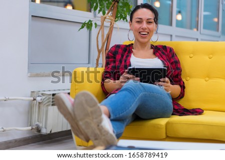 Young American business woman sitting at her sofa, using tablet in her office and smiling.
