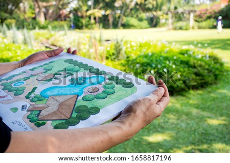 paper sheet of layout plan with hands and garden background, that shown design of clubhouse landscape or garden design   drawing by hand with color marker pens and color pencil, selective focus Royalty-Free Stock Photo #1658817196
