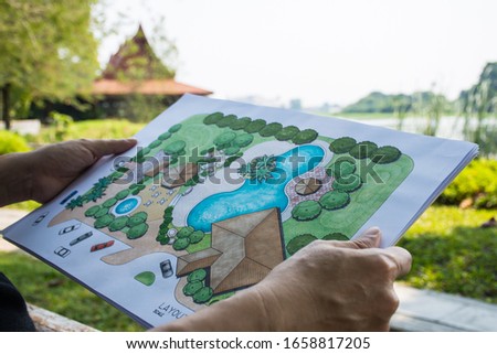 paper sheet of layout plan with hands and garden background, that shown design of clubhouse landscape or garden design   drawing by hand with color marker pens and color pencil, selective focus Royalty-Free Stock Photo #1658817205
