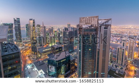 Skyline of the West Bay area from top in Doha night to day transition timelapse, Qatar. Illuminated modern skyscrapers aerial view from rooftop at morning before sunrise