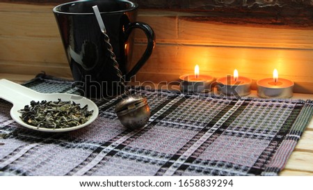 Burning candles against a wooden wall and tea items on checkered lilac fabric