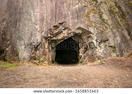 Rock wall with a dark hole, entrance to the cave in Spro, Mineral historic mine. Nesodden Norway. Nesoddtangen peninsula. Royalty-Free Stock Photo #1658851663