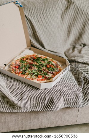 Pizza in opened box with arugula and tomatoes. 