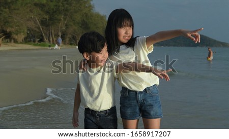 The sister pointed his brother to look at the waves breaking into the beach.