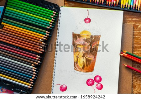 Pencil color tray on the side and half done pencilcolor hand drawing in white paper sketchbook. Chocobanana milkshake in pencil color.