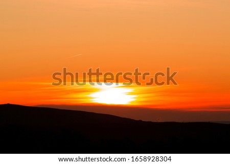 Sun hidden by a soft cloud with silhouette of mountains.
