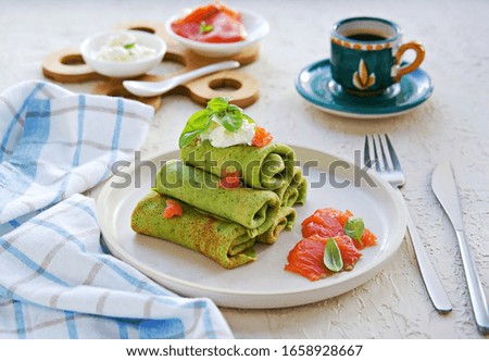 Spinach pancakes rolled up on a white plate on a light concrete background. Served with salted salmon and soft cheese. Spinach recipes.