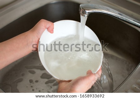 the child helps her mother around the house, washes white dishes under the tap of tap water. photo cropped.