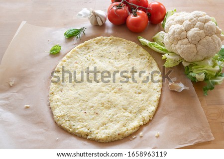 raw pizza base from shredded cauliflower on baking paper, healthy vegetable alternative for low carb and ketogenic diet, copy space, selected focus, narrow depth of field Royalty-Free Stock Photo #1658963119