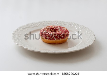 American donut with pink frosting sprinkled with pieces of white chocolate on a white decorative plate