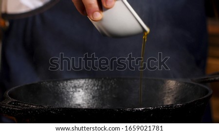 Pouring cooking oil into frying pan. Stock footage. Close up of chef male hands adding golden vegetable oil into black iron pan for cooking.