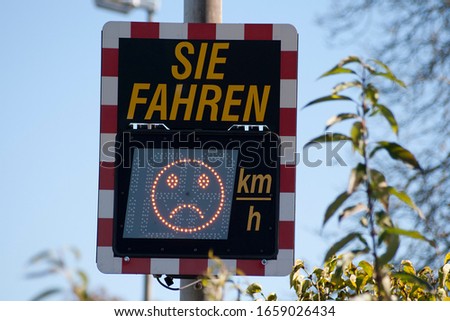 Digital speed limit sign in germany shows car driver speed measurement. (Translation "you drive... mp/h") Driver can see in Display his Speed and a happy  under limit or a sad face by driving too fast