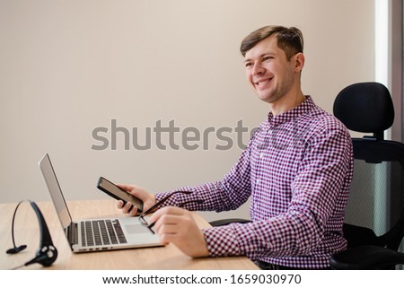 Close up face of young handsome man with casual shirt holding glasses and smartphone and smile in the office.