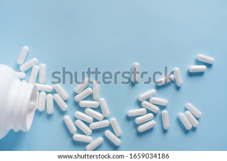 Top view of capsules spilling from white container. Health care. Royalty-Free Stock Photo #1659034186