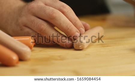 Close-up of man hands cutting sausages on a wooden chopping board with a kitchen knife. Stock footage. Preparing food.