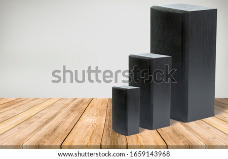 A studio shot of a three  black speakers with different sizes isolated on a empty room with wooden floor and  wall at the background.