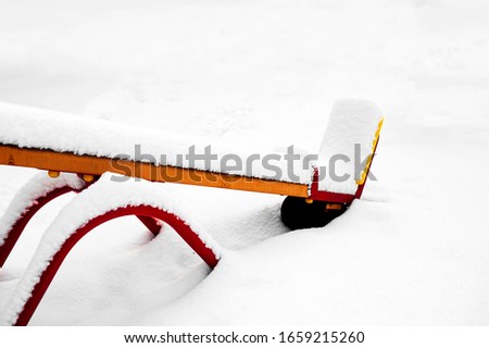 Fresh fluffy untouched snow on the children's bright yellow and red swing.