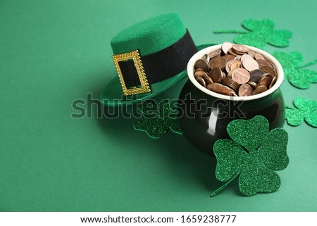 Pot of gold coins, hat and clover leaves on green background, space for text. St. Patrick's Day celebration