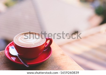 Closeup image of a red cup of hot latte coffee and milk bubble with latte art on wooden table, morning time
