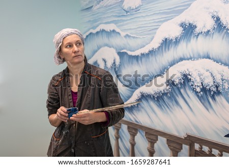 Female artist working on a mural on a marine theme. Portrait of the artist on the background of her work - mural