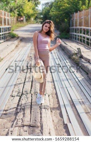 Warm summer portrait of a young beautiful woman wearing cowboy hat posing on the old rusty bridge during sunset.