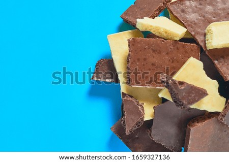 Heap of pieces various whole porous chocolate bars lies on blue table on kitchen. Space for text. Top view