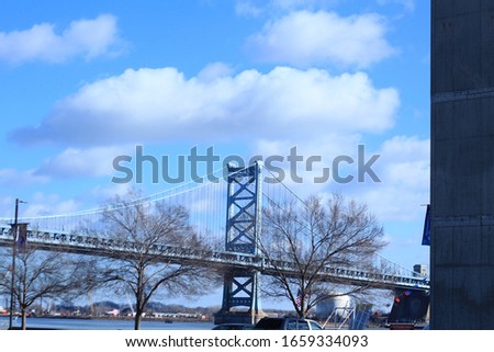 The Benjamin Franklin Bridge surrounded by trees and cars under a cloudy sky in Philadelphia